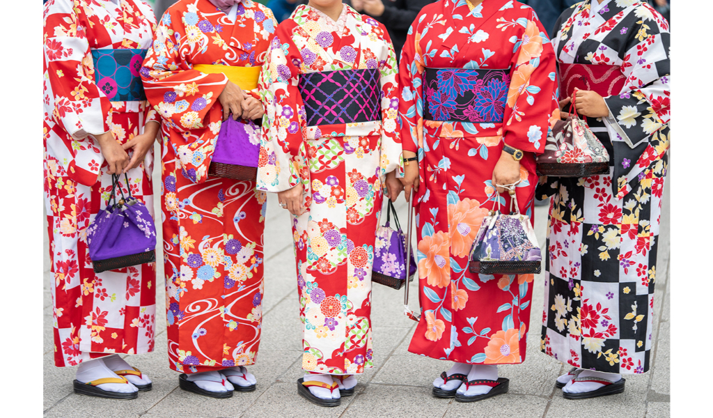 5 femmes portants un kimono rouge traditionnel prennent la pose. leur tête est coupée de sorte qu'on ne voit que leur kimono et leurs tongs chaussettes. elles portent également un petit sac à main assortie à fleurs.