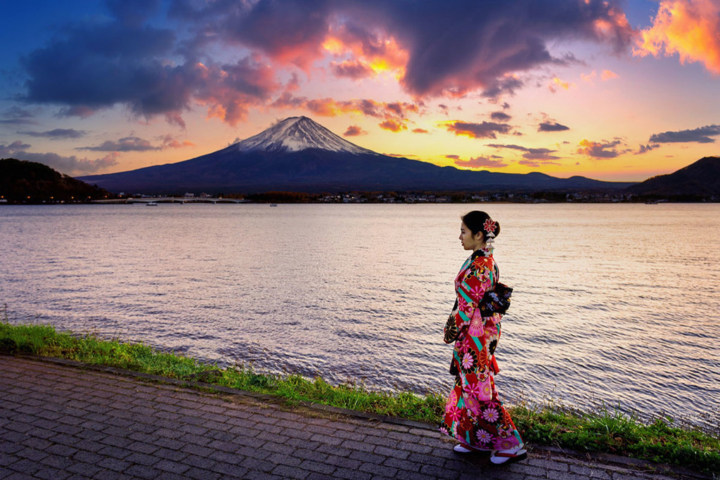 une femme d'origine asiatique en kimono traditionnel à fleurs marche le long de la mer avec une montagne enneigé en fond
