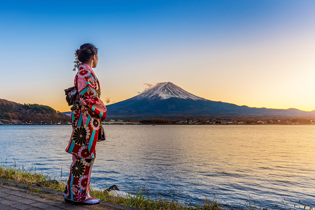 une femme d'origine asiatique en kimono traditionnel regarde une montagne enneigée devant une grande étendue d'eau
