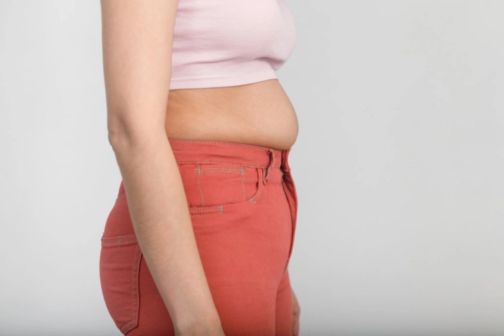 vue sur le profil d'une femme avec un petit ventre qui dépasse de son pantalon en jean orange.