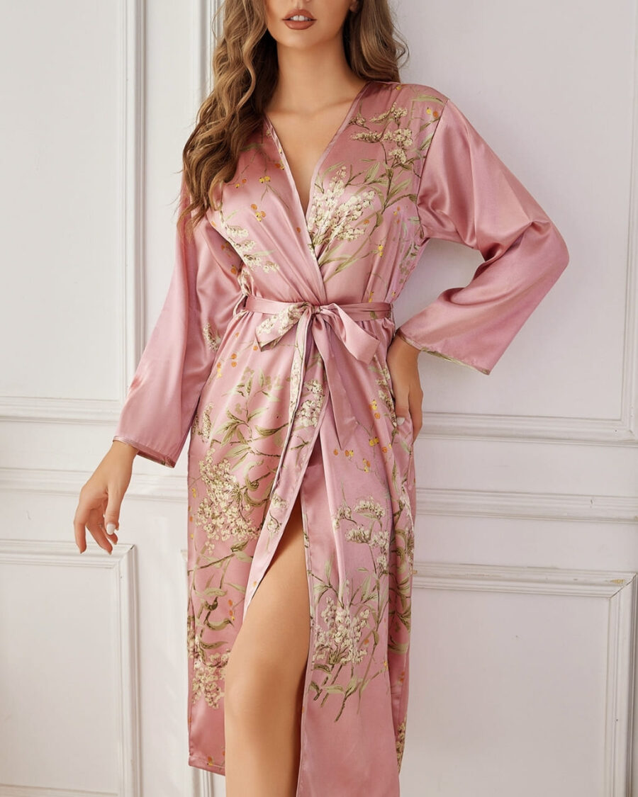 Long kimono coréen fleuri rose porté par une femme blonde contre un mur blanc.