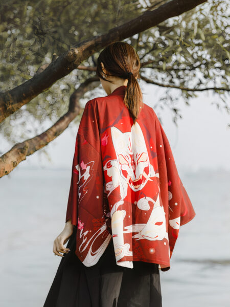 Une femme de dos dans la nature porte un kimono rouge avec un motif de tête de chat mort blanc et une paysage japonaise