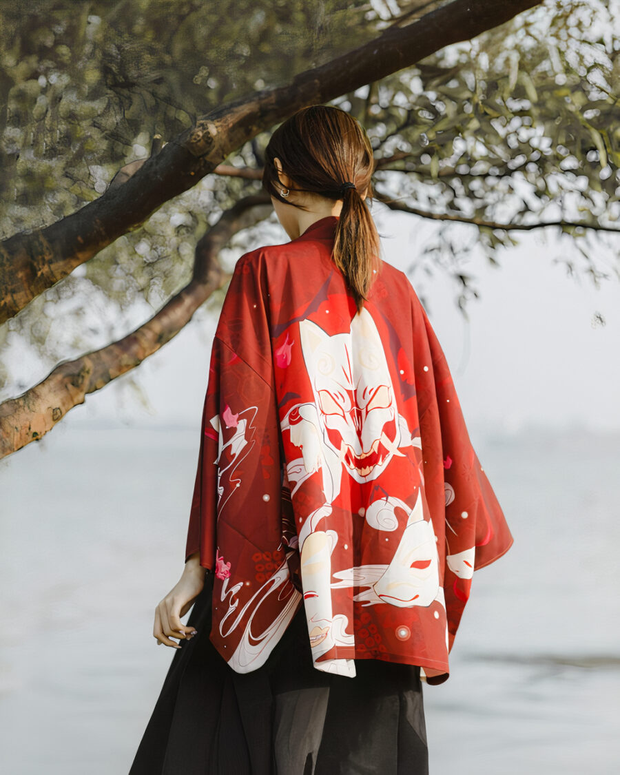 Une femme de dos dans la nature porte un kimono rouge avec un motif de tête de chat mort blanc et une paysage japonaise