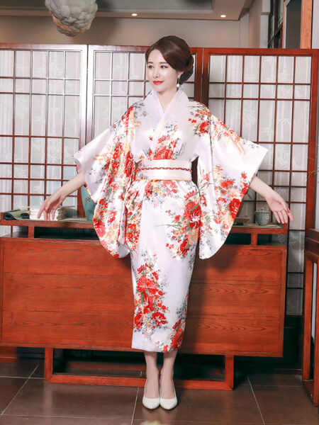 Femme de tipe asiatique portant un kimono traditionnel, floral, blanc et rouge se tenant debout dans un salon japonais.