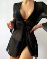 Une femme porte un kimono transparent noir court sur un maillot de bain noir. Elle tire la corde qui tient le kimono.