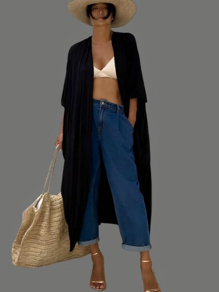 Kimono long noir à ceinture pour femme porté par une jeune femme, qui porte également un chapeau de paille. Elle a son bikini en dessous du kimono et porte à la main droite un grand sac cabas en paille beige.