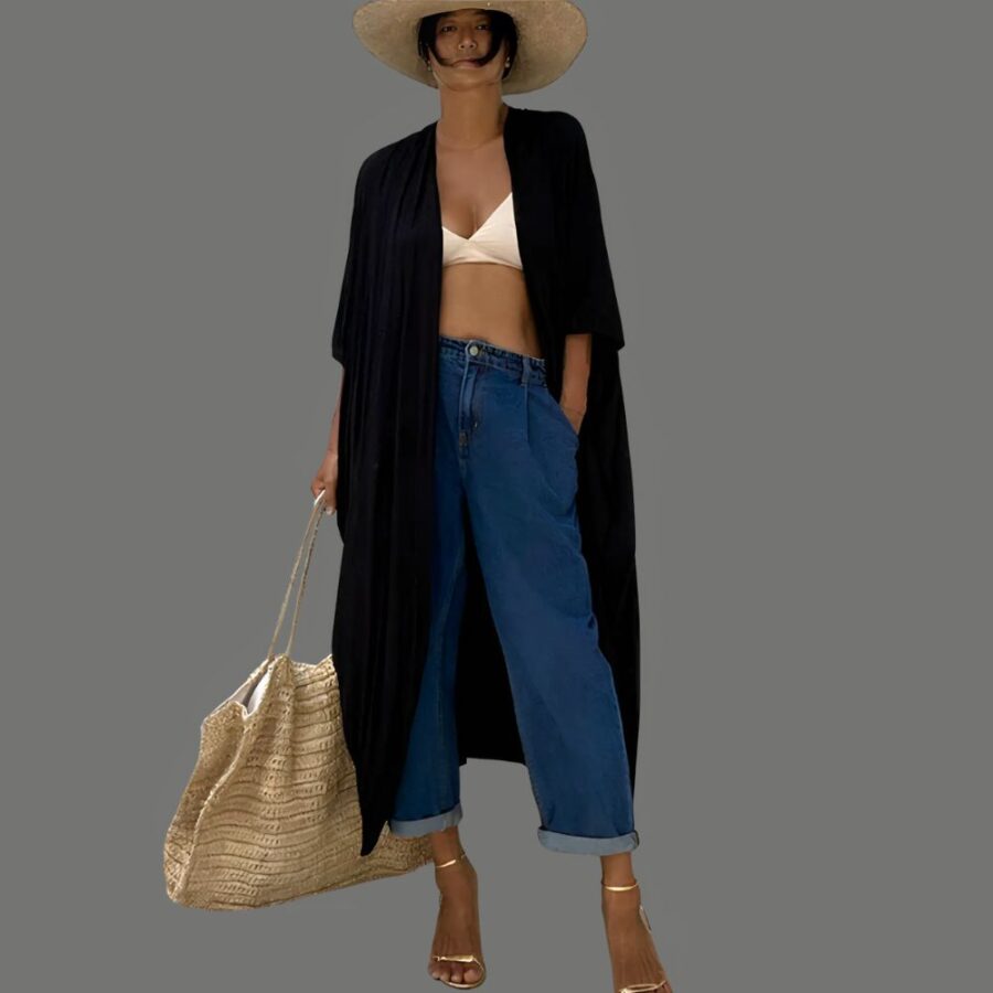 Kimono long noir à ceinture pour femme porté par une jeune femme, qui porte également un chapeau de paille. Elle a son bikini en dessous du kimono et porte à la main droite un grand sac cabas en paille beige.