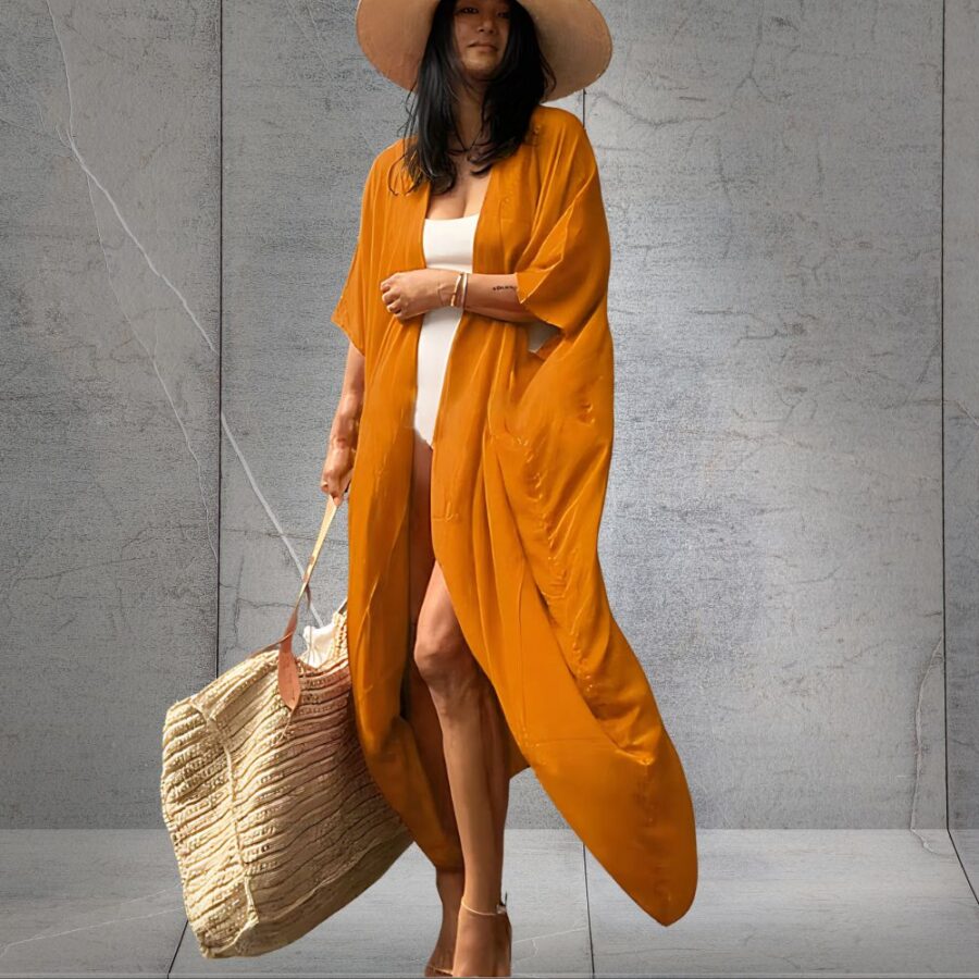 Kimono long orange à ceinture pour femme porté par une jeune femme brune portant un chapeau et un grand sac en paille, sur fond gris.