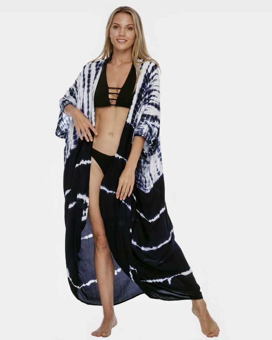 Jeune femme blonde en bikini qui porte un kimono blanc et le bas noir style bohème, qui a sa main droite sur la taille