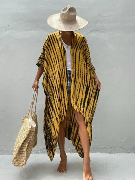 Femme portant un kimono jaune à pois noir disposé en ligne verticale, elle porte un haut blanc, un sac en osier de plage, et un chapeau, elle regarde vers le bas et on ne voit pas son visage