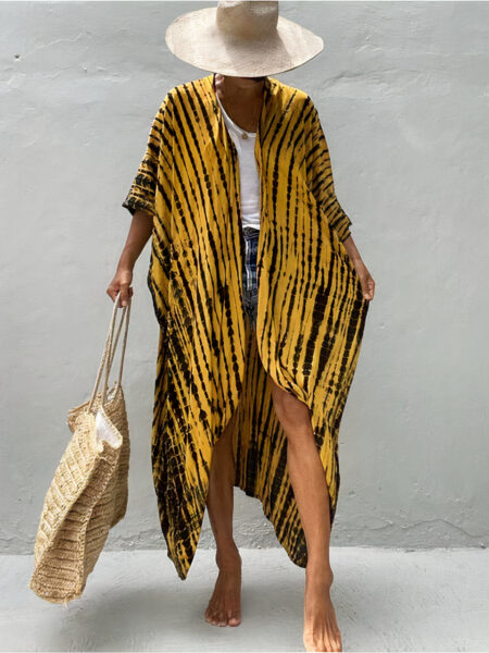 Femme portant un kimono jaune à pois noir disposé en ligne verticale, elle porte un haut blanc, un sac en osier de plage, et un chapeau, elle regarde vers le bas et on ne voit pas son visage