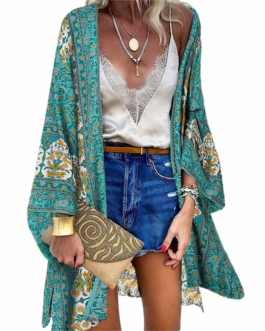 Femme blonde dont on ne voit pas la tête qui porte un short en jean, un débardeur à dentalle blanc, par dessus lequel elle à un kimono bohème bleu , elle a également un gros bracelet couleur or et une pochette à la main droite