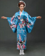 Une femme porte un kimono bleu turquoise avec des motifs japonais à manches larges, ses cheveux sont coiffés en chignons traditionnels, ses bras son ouverts de part et d'autre