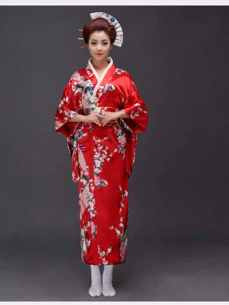 Une femme porte un kimono rouge avec des motifs japonais à manches larges, ses cheveux sont coiffés en chignons traditionnels, elle tient ses mains devant elle