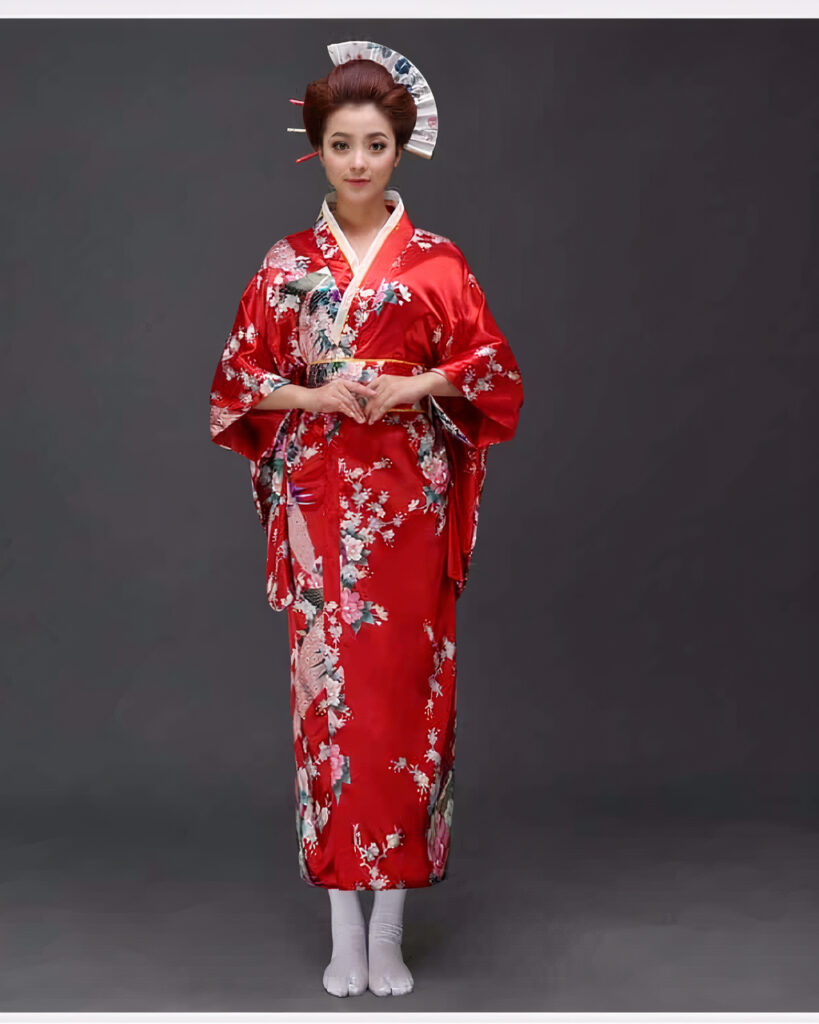 Une femme porte un kimono rouge avec des motifs japonais à manches larges, ses cheveux sont coiffés en chignons traditionnels, elle tient ses mains devant elle