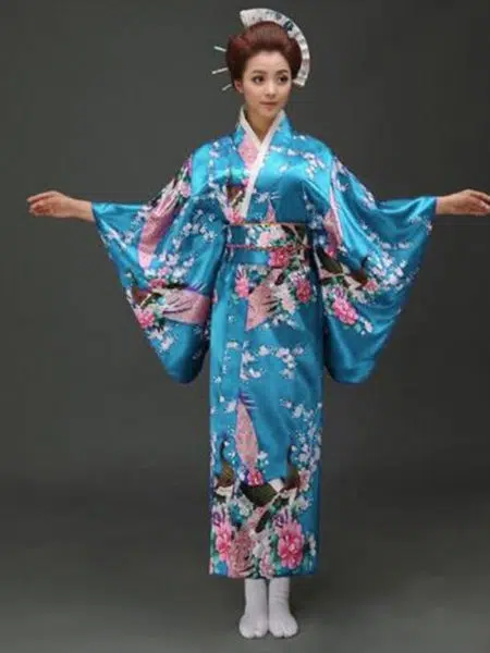 Une femme porte un kimono bleu turquoise avec des motifs japonais à manches larges, ses cheveux sont coiffés en chignons traditionnels, ses bras son ouverts de part et d'autre