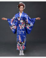 Une femme porte un kimono bleu avec des motifs japonais à manches larges, ses cheveux sont coiffés en chignons traditionnels, ses bras son ouverts de part et d'autre