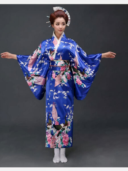 Une femme porte un kimono bleu avec des motifs japonais à manches larges, ses cheveux sont coiffés en chignons traditionnels, ses bras son ouverts de part et d'autre