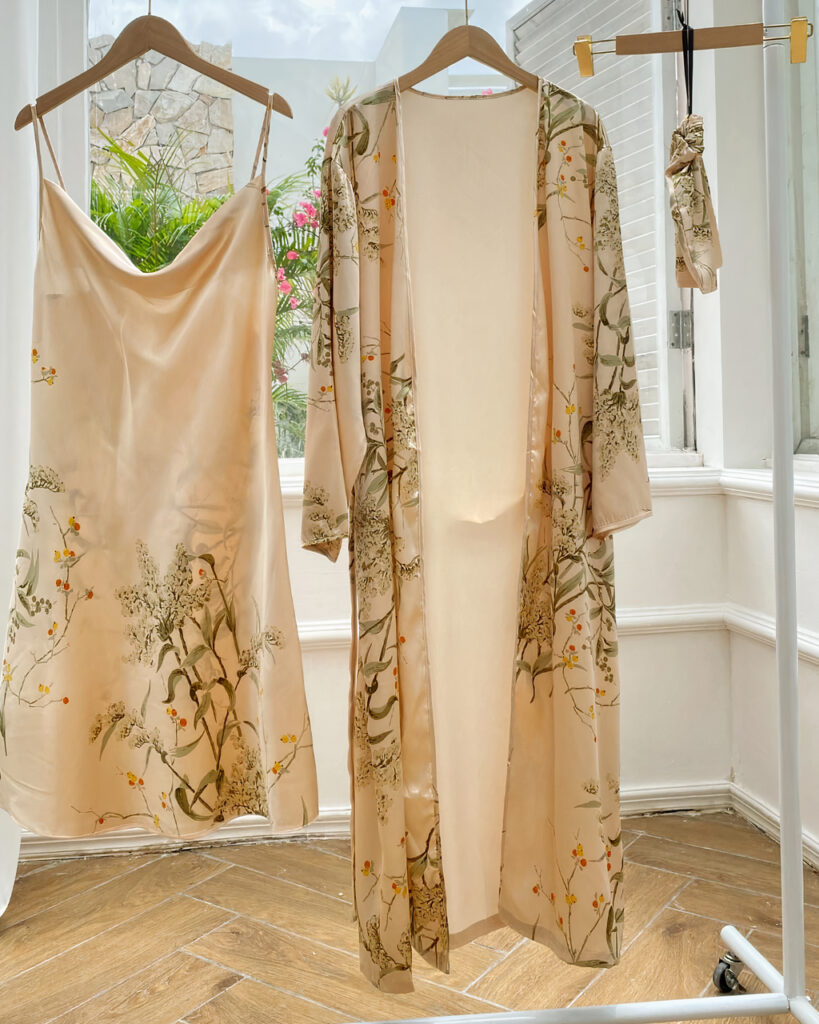 Ensemble nuisette et kimono beige à imprimé floral suspendus à des cintres dans une pièce avec parquet et mur blanc et devant une fenêtre ouverte