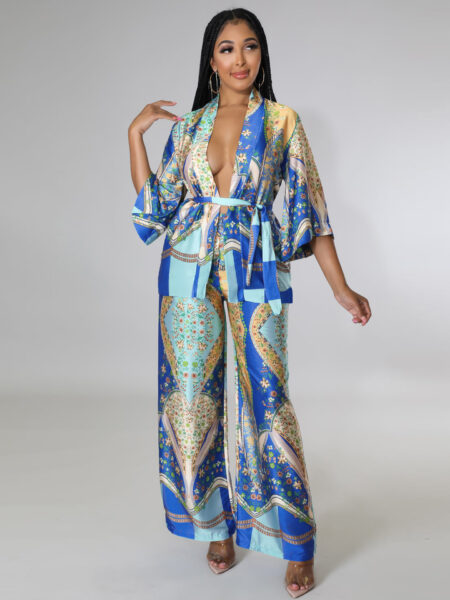 Ensemble pantalon kimono en satin de couleur bleu avec des motifs floraux verts et dorés porté par une femme devant un mur gris