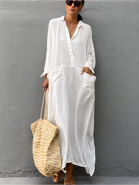 Tunique pour plage blanche portée par une femme avec des lunettes noires et un sac en paille devant un mur gris