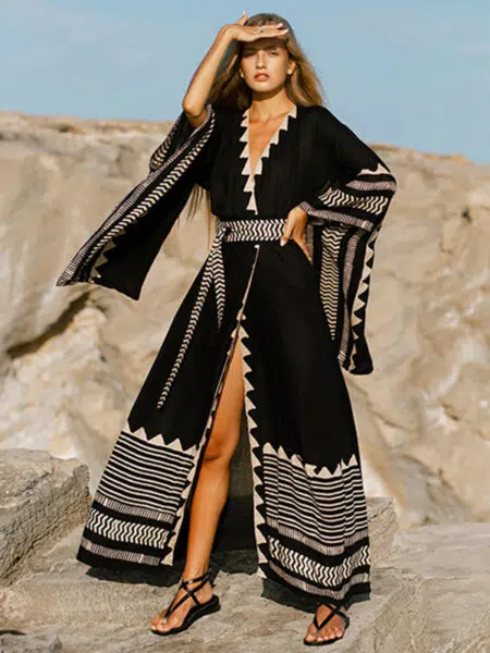 Une femme sur un rocher regardant a l'horizon. Elle porte un long kimono noir de plage avec des motifs géométriques blanc. Il est fermé par une ceinture en tissus dans le même coloris.