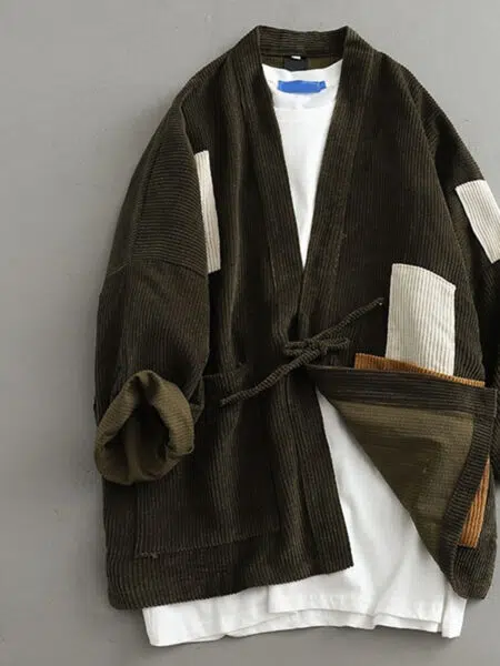 Un kimono en velours côtelé de couleur noire, il a des parties rapiécées de couleur noire et blanche. Il a une ceinture dans le même coloris pour le fermer.