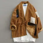 Un kimono en velours côtelé de couleur marron, il a des parties rapiécé de couleur noire et blanche. Il a une ceinture dans le même coloris pour le fermer.