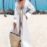 sur un plage une femme porte un kimono en dentelle blanc avec motifs découpés, et un sac en osier et un chapeau blanc