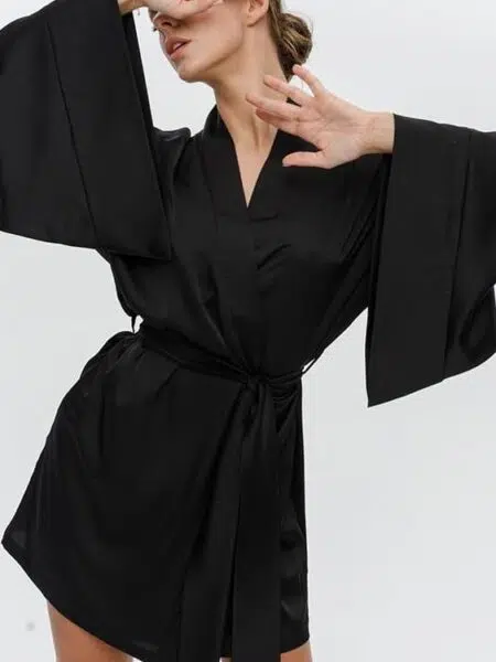 jeune femme blonde qui porte un kimono peignoir en satin noir et elle tient les mains devant son visage