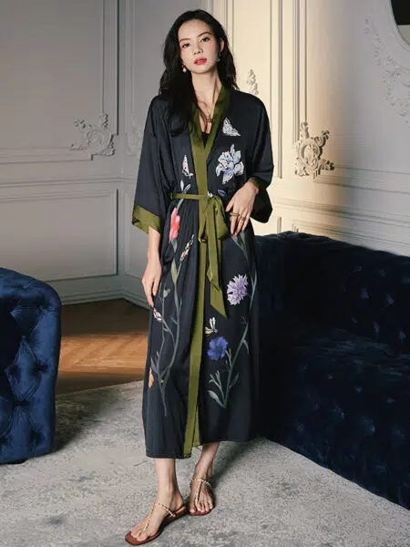 dans une pièce avec moulures, une jeune femme asiatique porte un kimono en satin noir avec bordures vertes foncées et des motifs de fleurs
