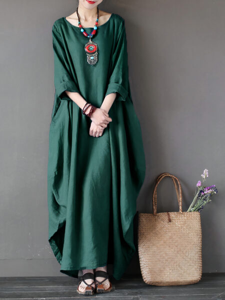 Robe kimono longue ample verte portée par une femme appuyé dos au mur, avec un sac posé au sol près d'elle