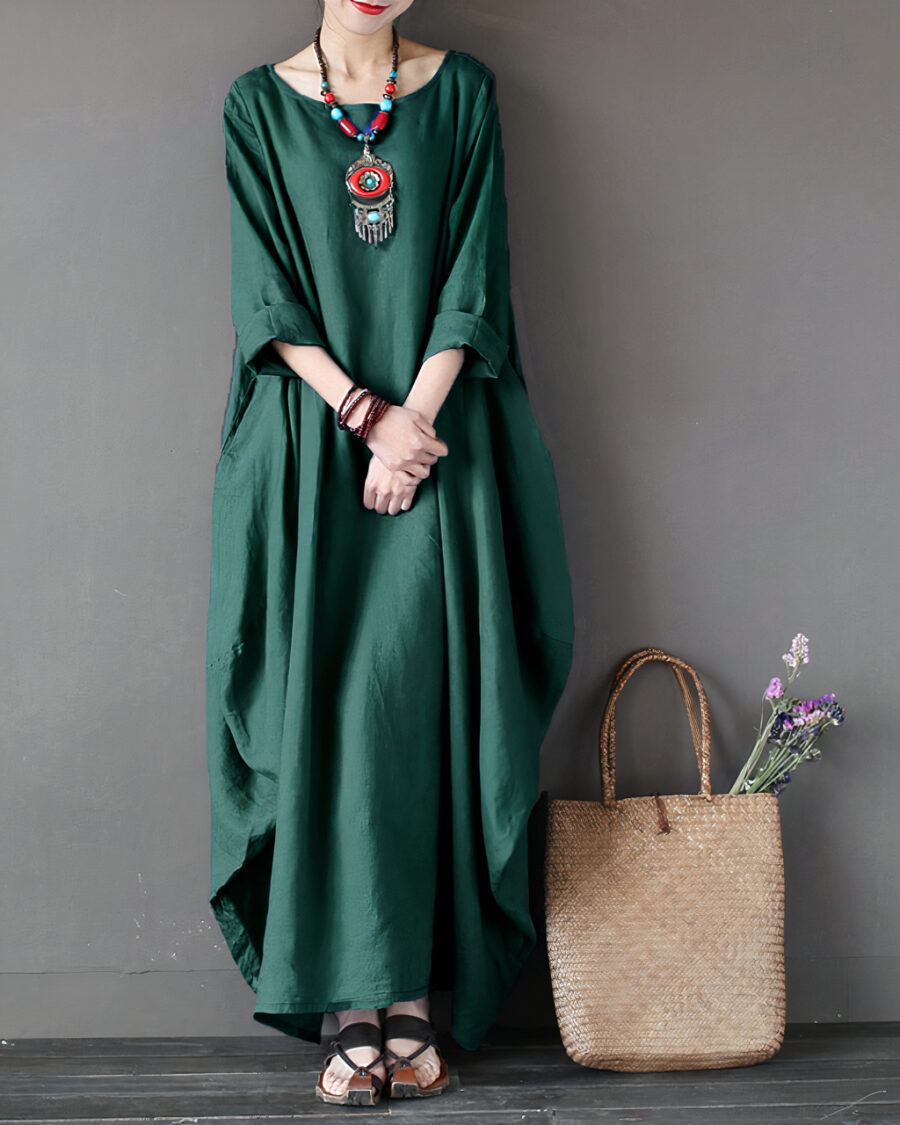 Robe kimono longue ample verte portée par une femme appuyé dos au mur, avec un sac posé au sol près d'elle